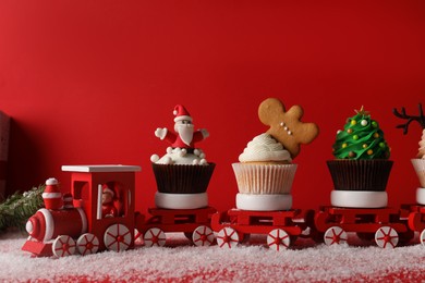 Photo of Toy train with tasty Christmas cupcakes on red background