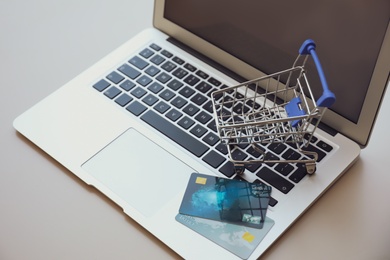 Photo of Internet shopping. Modern laptop with small cart and credit cards on light table