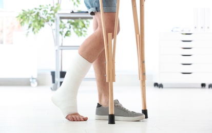 Photo of Man with broken leg in cast standing on crutches, indoors