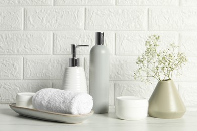 Photo of Different bath accessories, personal care products and gypsophila flowers in vase on white table near brick wall