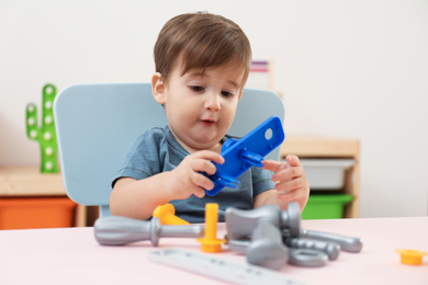 Little child playing with toy construction tools at table