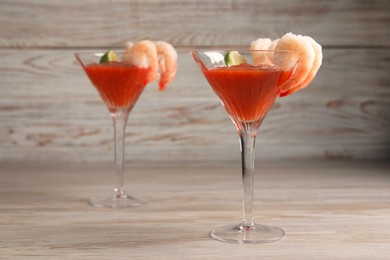 Photo of Tasty shrimp cocktail with sauce and lime in glasses on wooden table