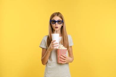 Photo of Emotional teenage girl with 3D glasses, popcorn and beverage during cinema show on color background