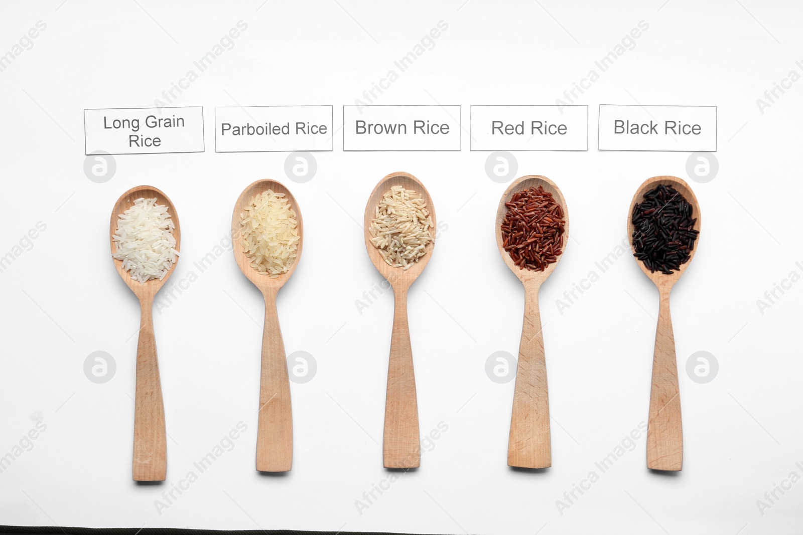 Photo of Spoons with different types of uncooked rice and cards on white background, top view