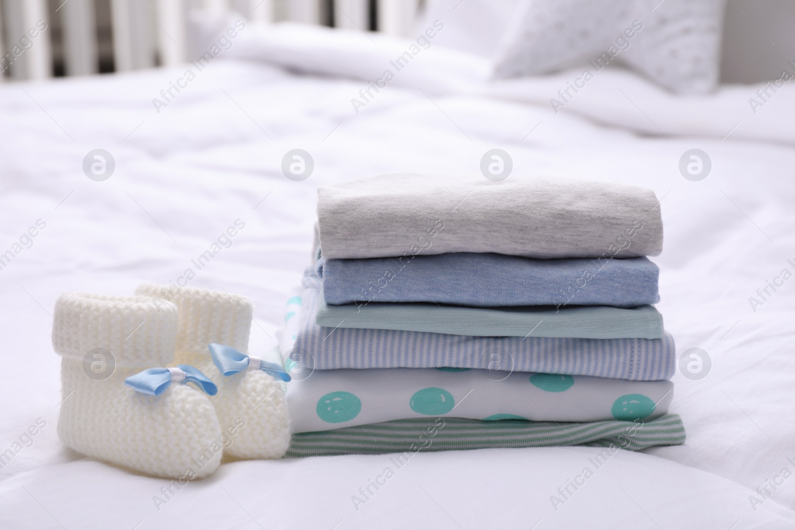 Photo of Stack of clean baby's clothes and small booties on bed
