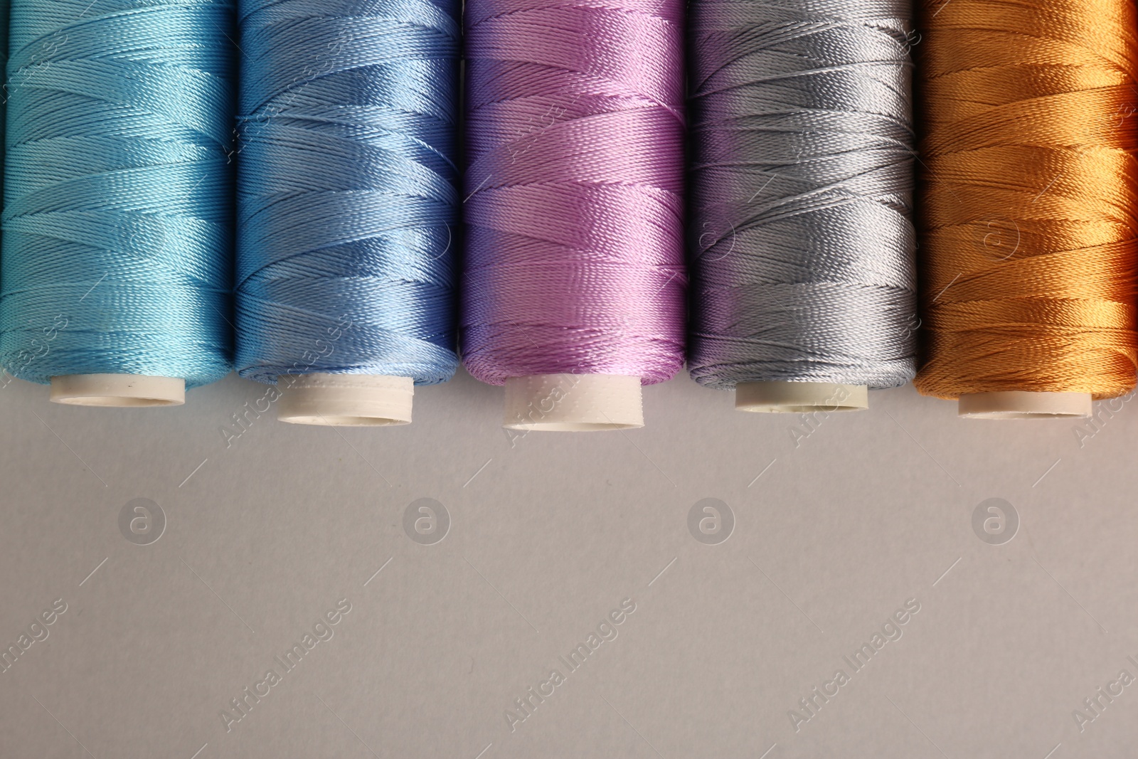 Photo of Different colorful sewing threads on light grey background, flat lay. Space for text