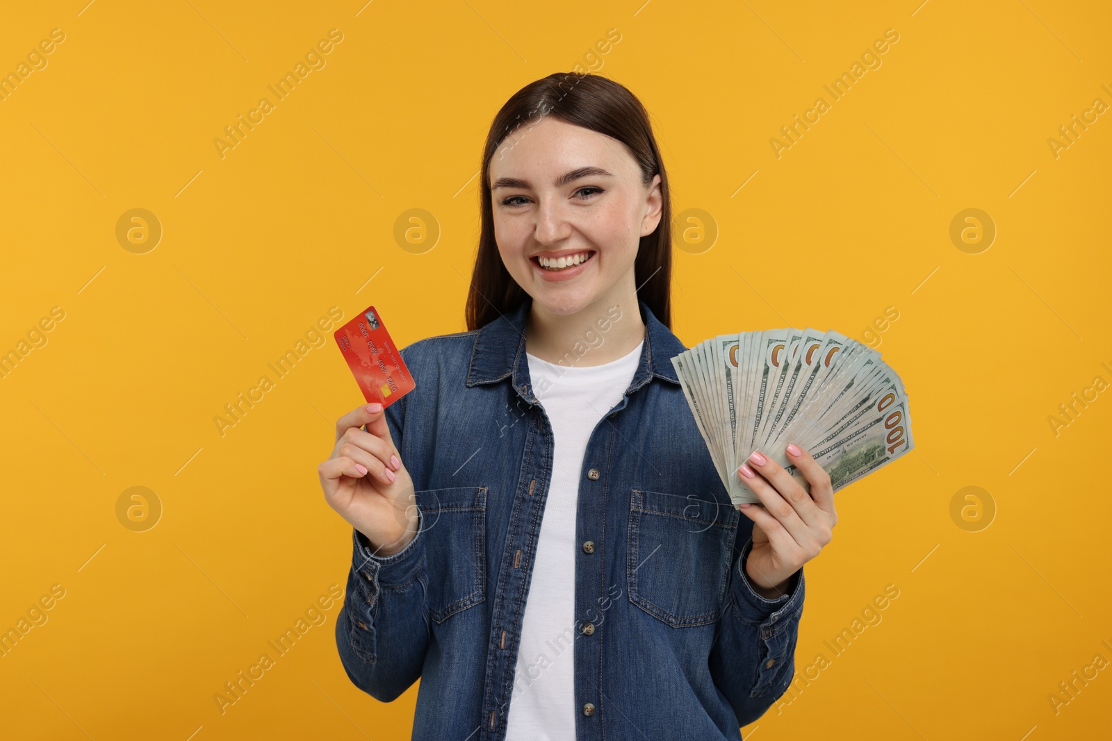 Photo of Happy woman with credit card and dollar banknotes on orange background