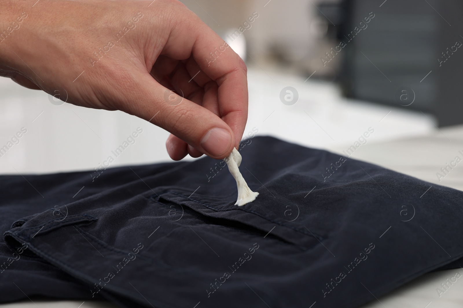 Photo of Man removing chewing gum from black jeans indoors, closeup. Space for text