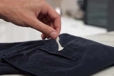 Man removing chewing gum from black jeans indoors, closeup. Space for text