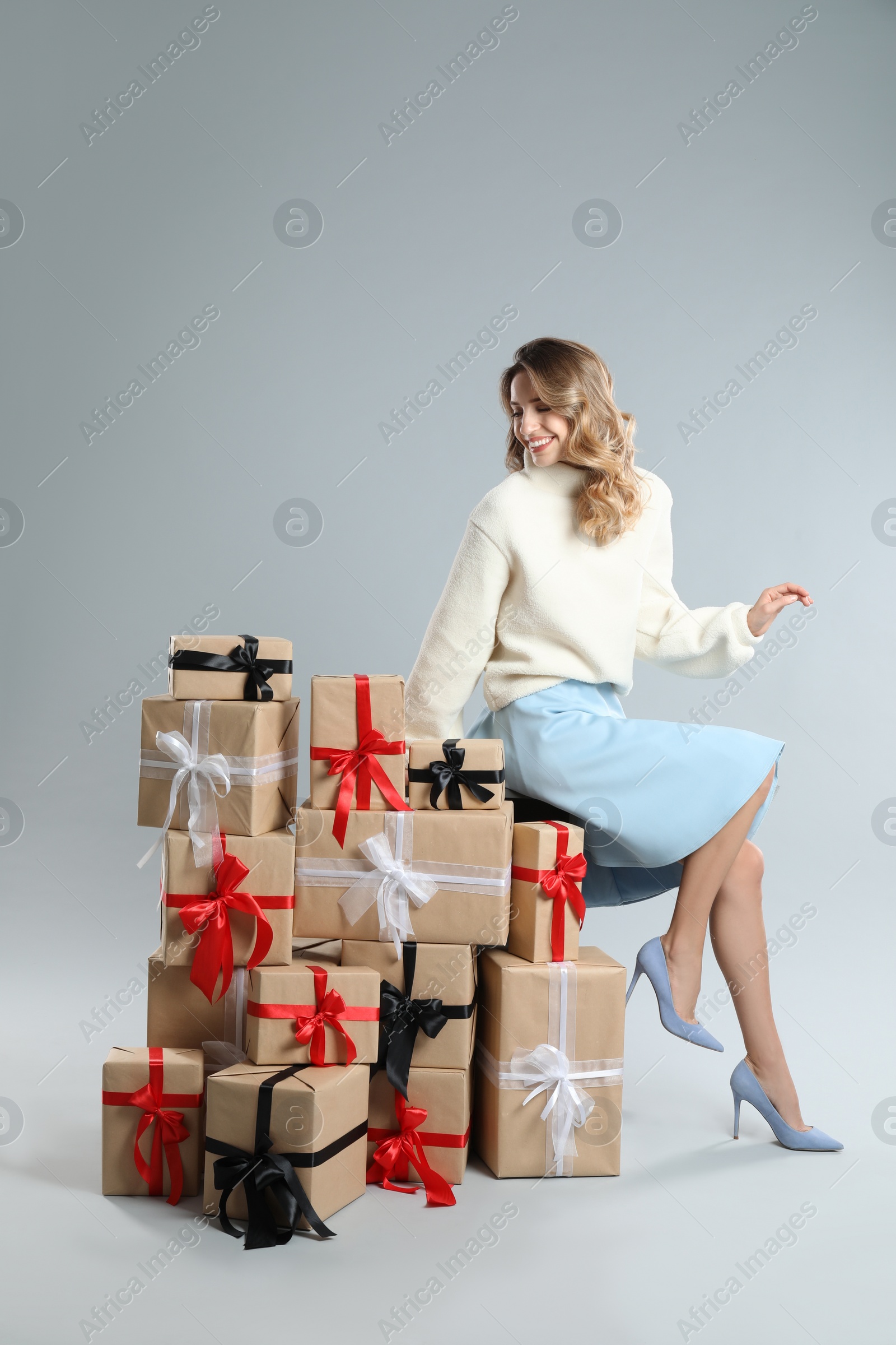 Photo of Beautiful young woman with pile of Christmas presents on light grey background