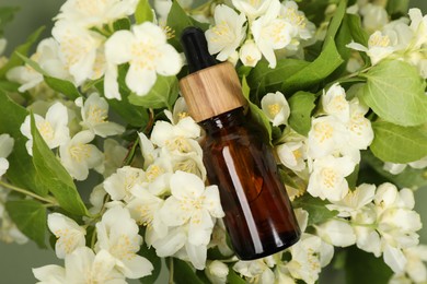 Photo of Essential oil in bottle on beautiful jasmine flowers against color background, flat lay