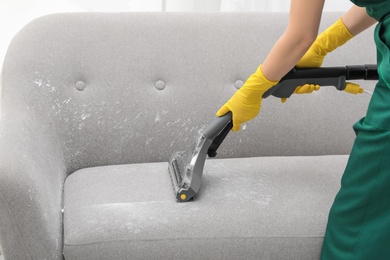 Janitor removing dirt from sofa with upholstery cleaner, closeup