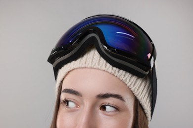 Winter sports. Happy woman with snowboard goggles on grey background, closeup