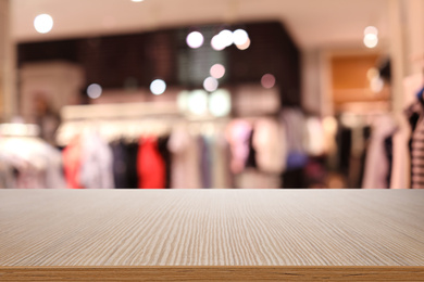 Empty wooden table and blurred view of store with modern clothes