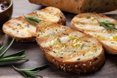 Tasty bruschettas with oil and rosemary on wooden table, closeup