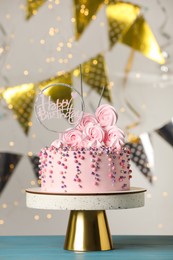 Beautifully decorated birthday cake and party decor on turquoise wooden table against blurred festive lights