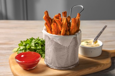 Photo of Frying basket with sweet potato fries, sauces and parsley on table
