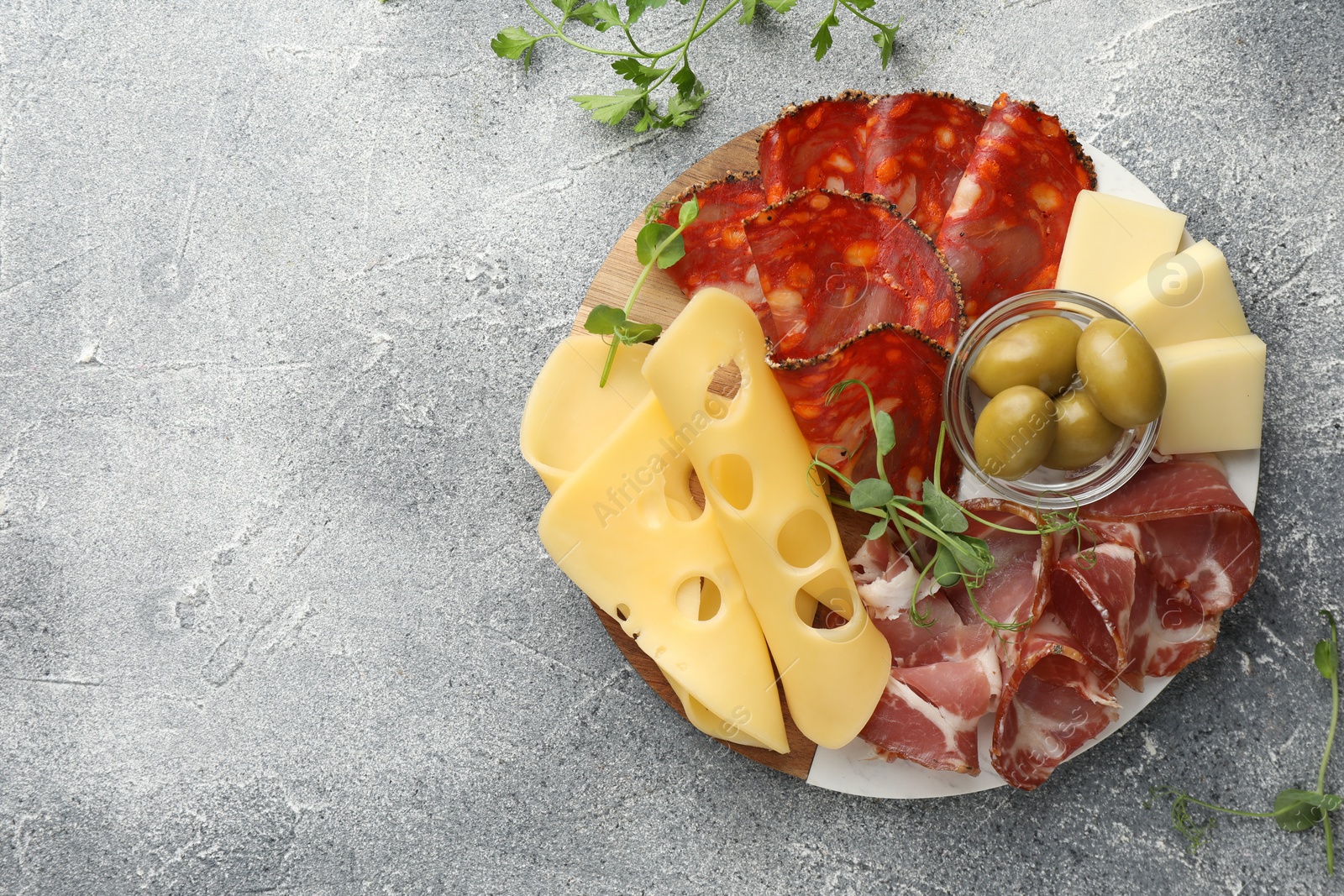 Photo of Serving board with delicious cured ham, cheese and olives on light grey table, flat lay. Space for text