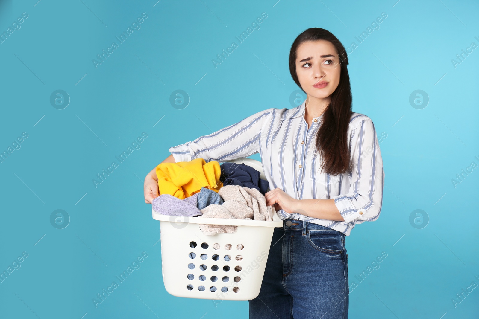 Photo of Displeased young woman holding basket with laundry on color background