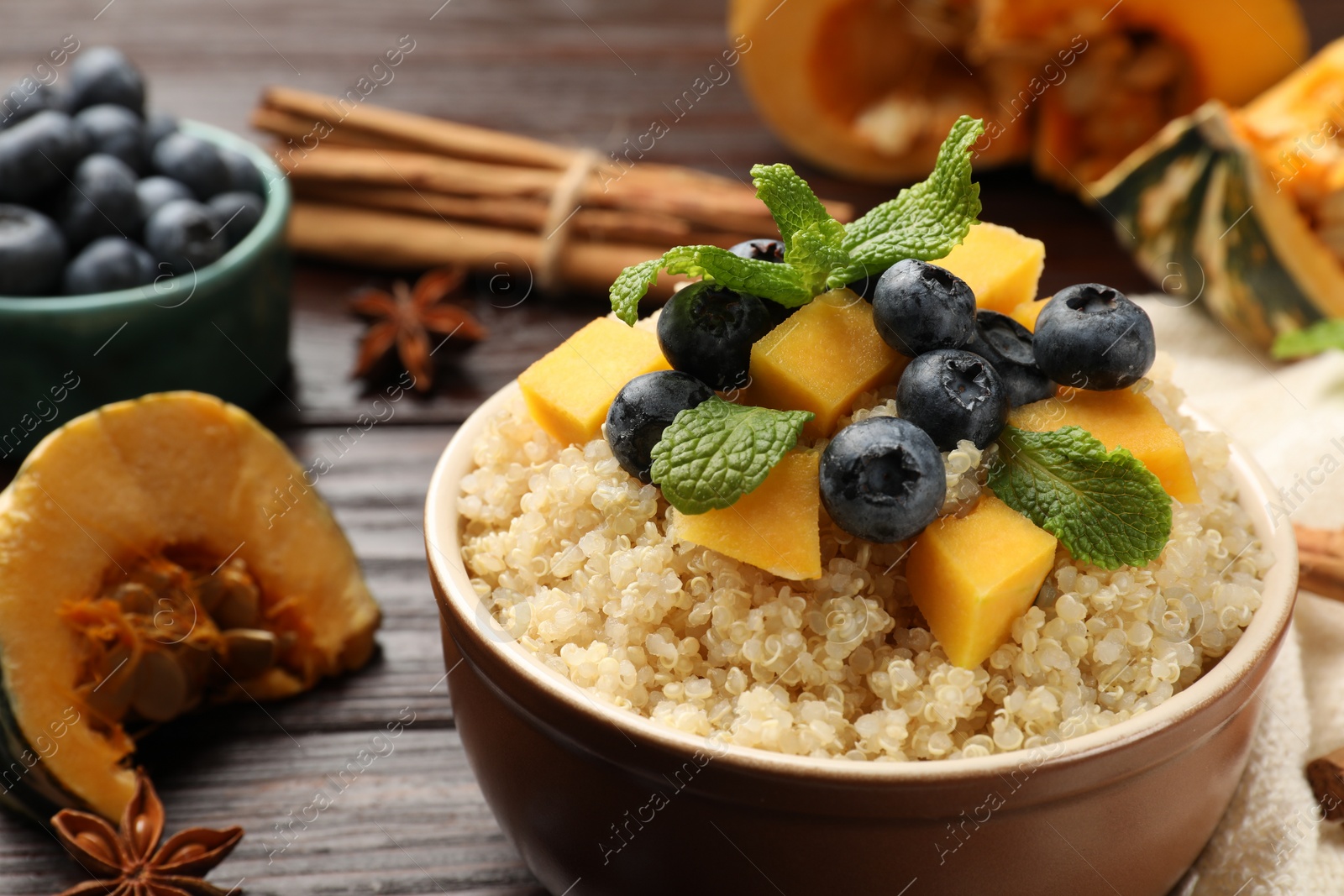 Photo of Tasty quinoa porridge with blueberries, pumpkin and mint in bowl on wooden table, closeup