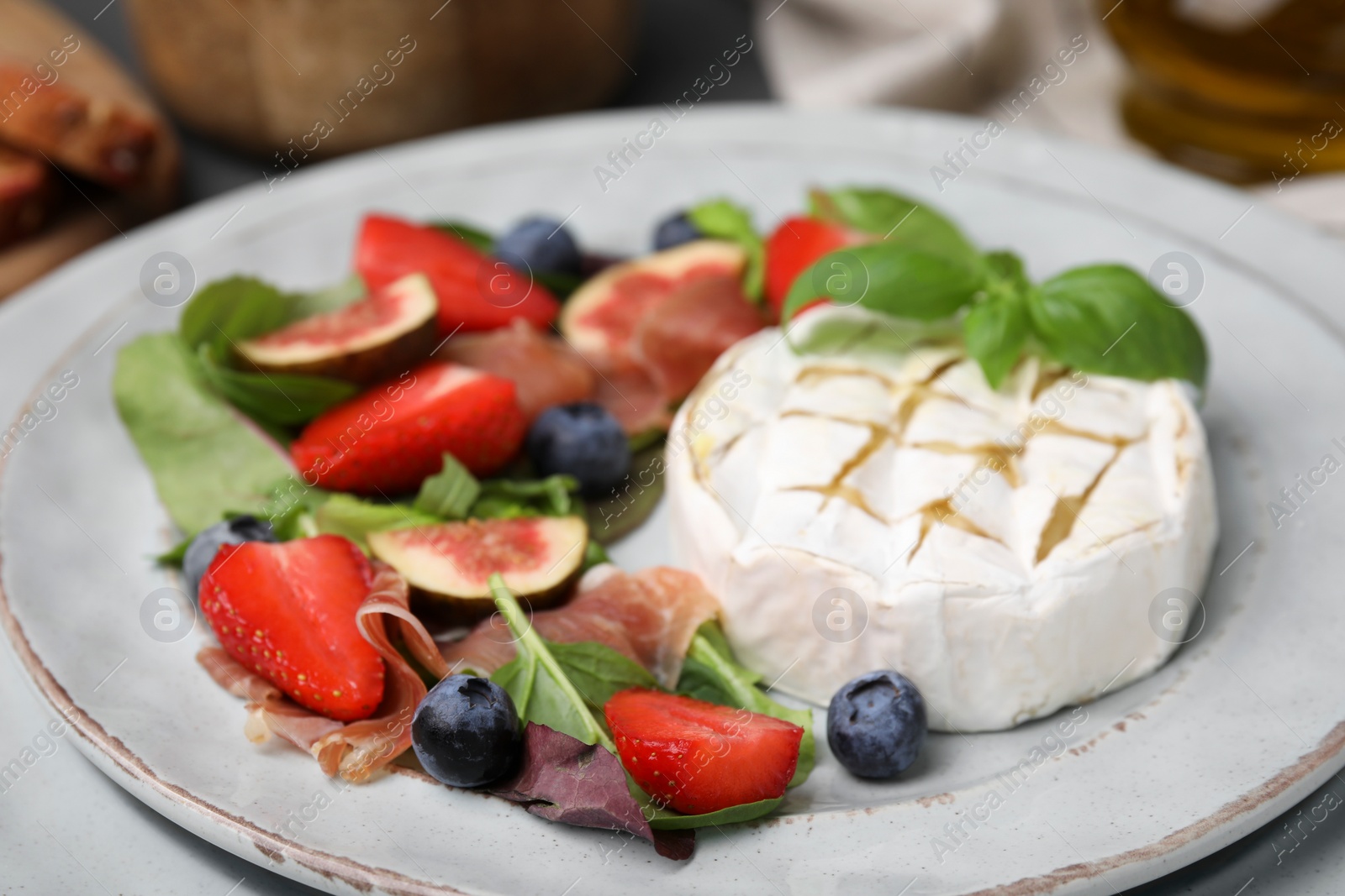 Photo of Delicious salad with brie cheese, prosciutto, strawberries and blueberries on plate, closeup