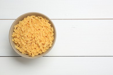 Photo of Raw farfalline pasta in bowl on white wooden table, top view. Space for text