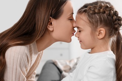 Photo of Happy mother kissing her cute daughter indoors, closeup