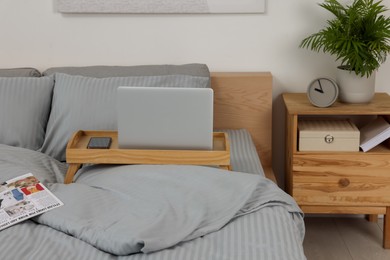 Photo of Wooden tray table with laptop and smartphone on bed indoors