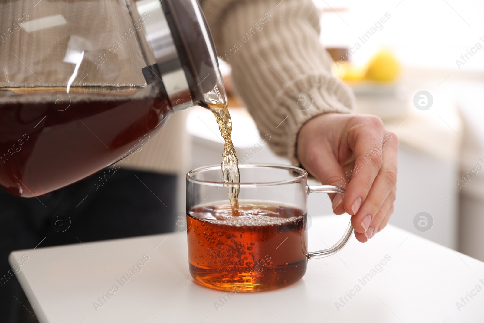 Photo of Woman pouring hot tea into cup at white table, closeup