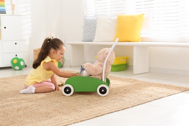 Photo of Cute little girl playing with toy walker and teddy bear at home