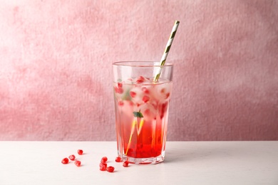 Tasty cocktail with pomegranate ice cubes on table against color background