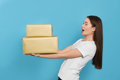 Photo of Emotional young woman with gift boxes on light blue background