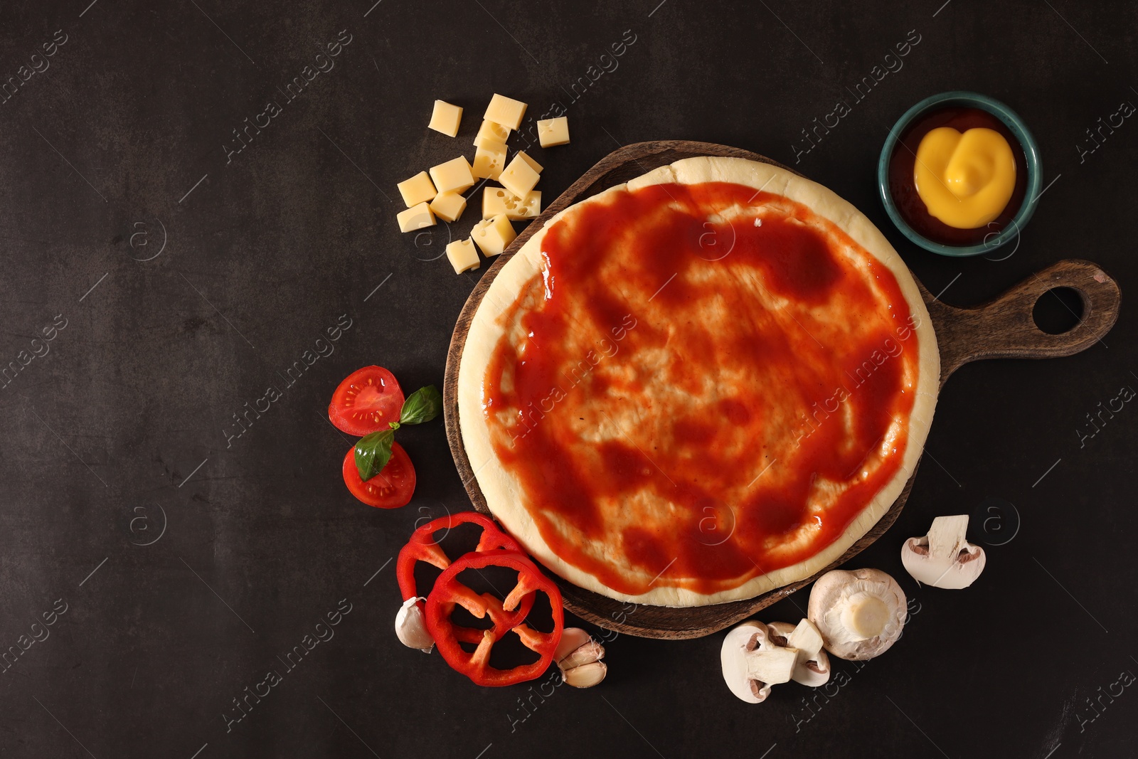 Photo of Pizza dough smeared with tomato sauce and products on dark table, flat lay. Space for text