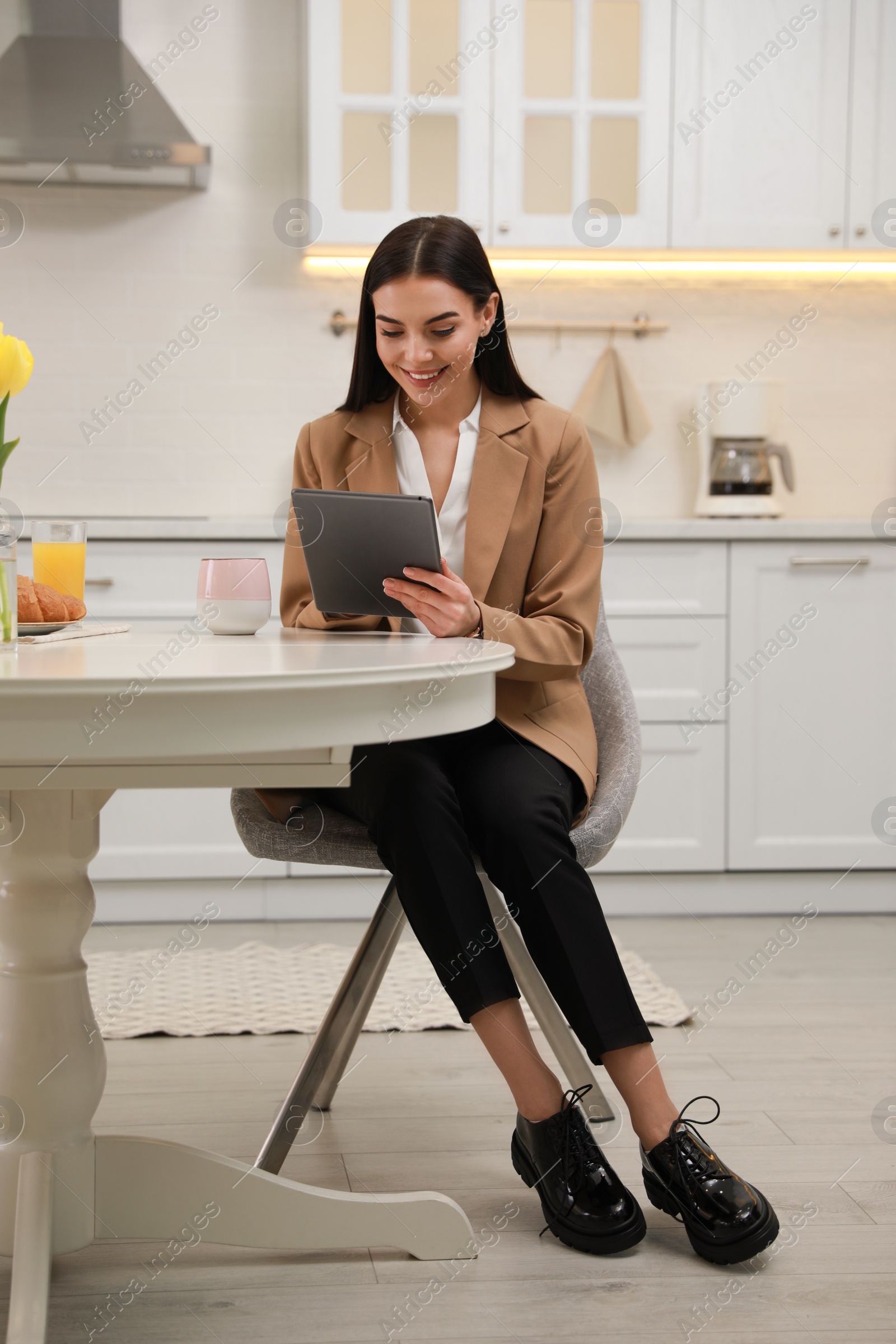 Photo of Young woman with tablet having breakfast in kitchen. Morning routine