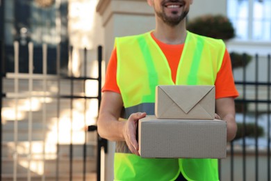 Courier in uniform with parcels outdoors, closeup. Space for text