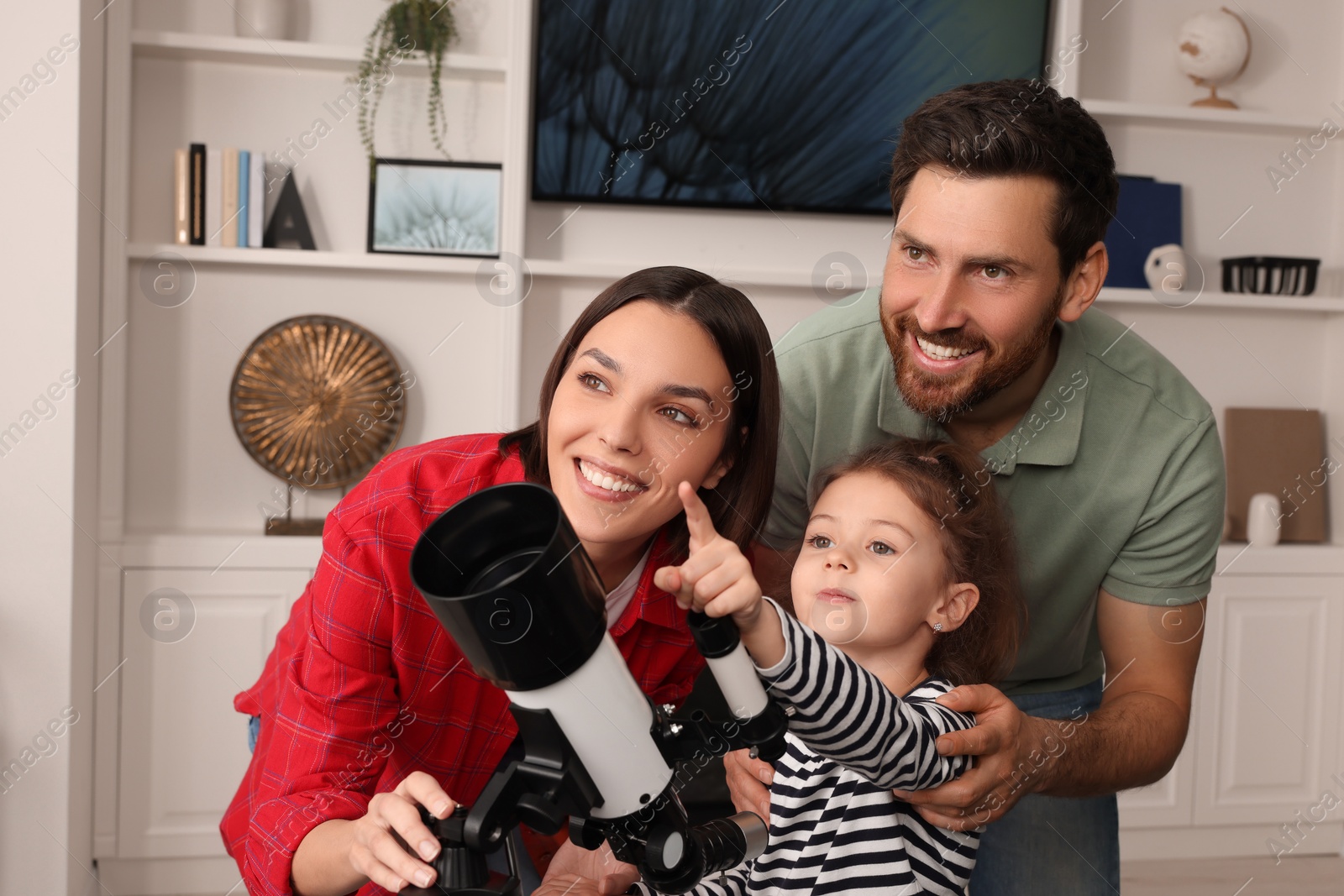 Photo of Happy family using telescope to look at stars in room