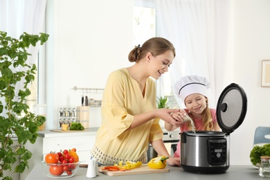 Photo of Mother and daughter preparing food with modern multi cooker in kitchen