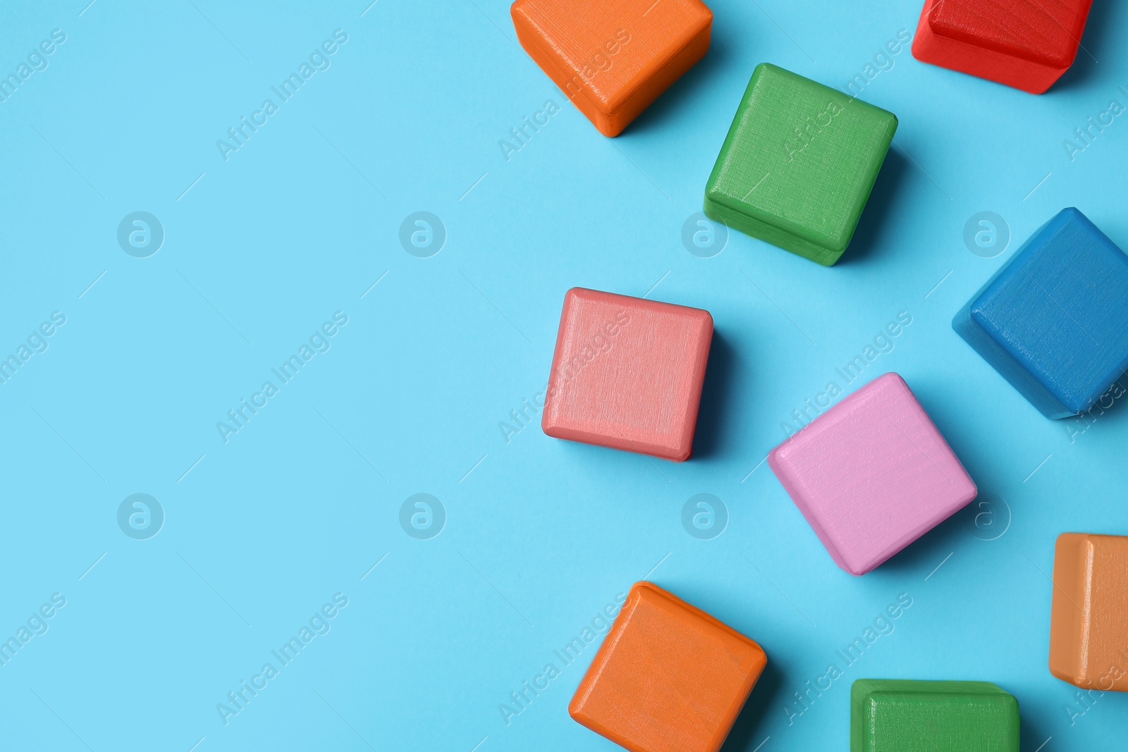 Photo of Blank colorful cubes on light blue background, flat lay. Space for text