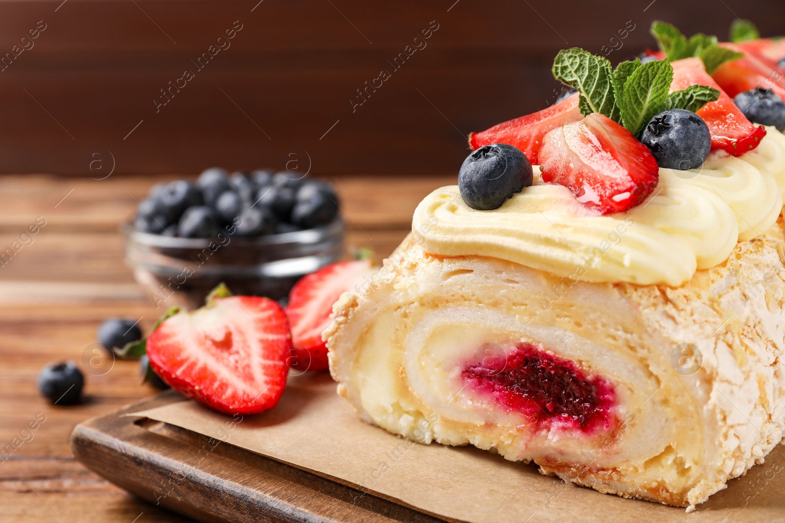 Photo of Tasty meringue roll with jam, cream, strawberry, blueberry and mint on wooden table, closeup
