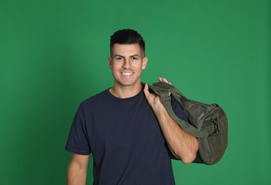 Handsome man with sports bag on green background