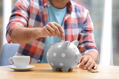 Man putting money into piggy bank at table, closeup