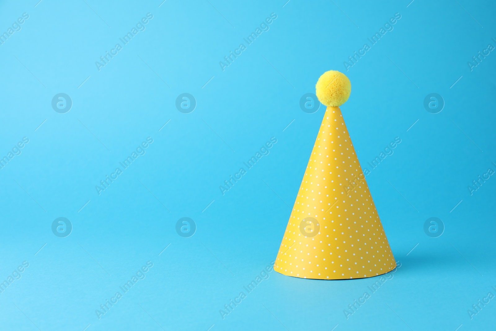 Photo of Yellow party hat on light blue background, space for text