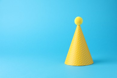 Photo of Yellow party hat on light blue background, space for text