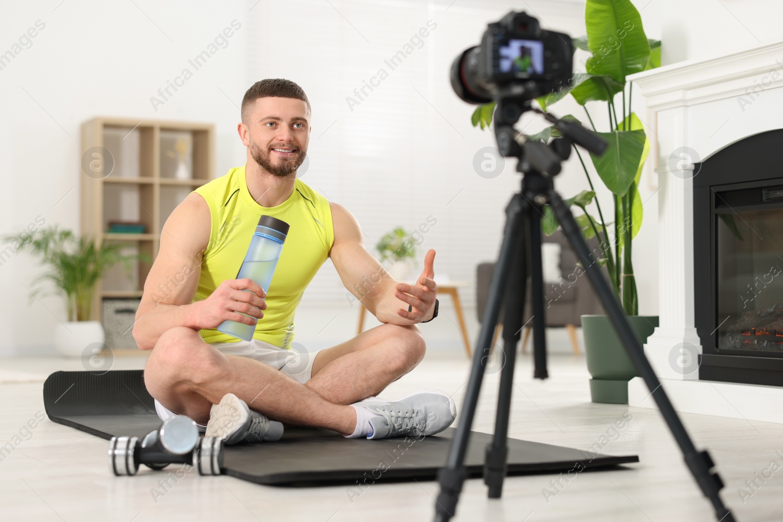 Photo of Trainer with bottle of water recording fitness lesson on camera at home