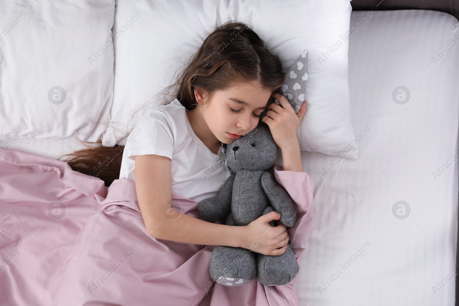 Photo of Beautiful little girl with toy rabbit sleeping in bed, top view
