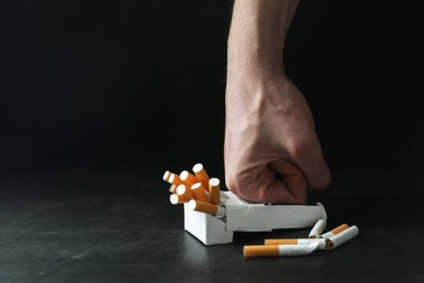 Photo of Stop smoking. Man crushing pack with cigarettes on dark background, closeup. Space for text