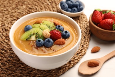 Photo of Delicious smoothie bowl with fresh berries, kiwi and nuts on table, closeup
