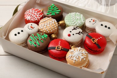 Photo of Beautifully decorated Christmas macarons in box on white wooden table, closeup