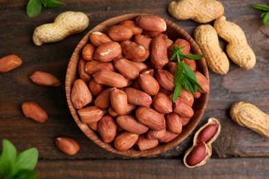 Fresh peanuts and leaves in bowl on wooden table, flat lay