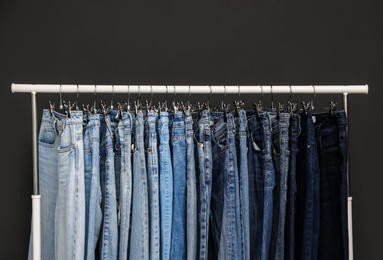 Photo of Rack with different jeans on dark grey background